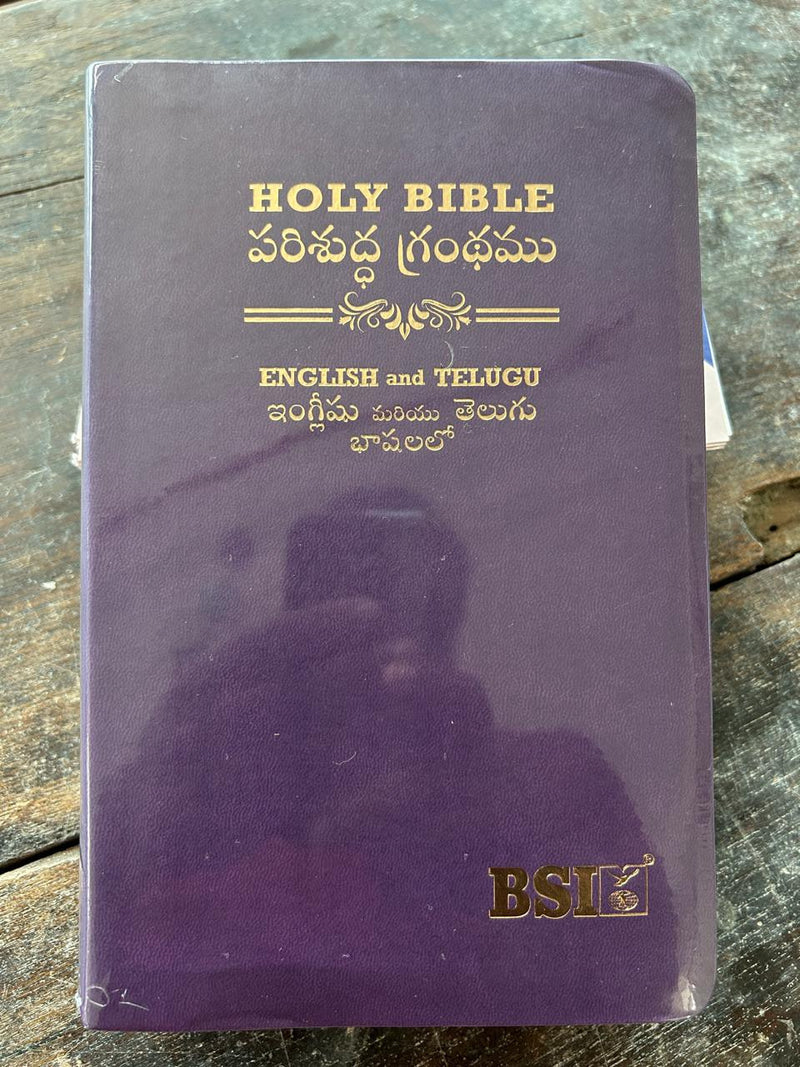 Purple Bible with English and Telugu text on a wooden surface